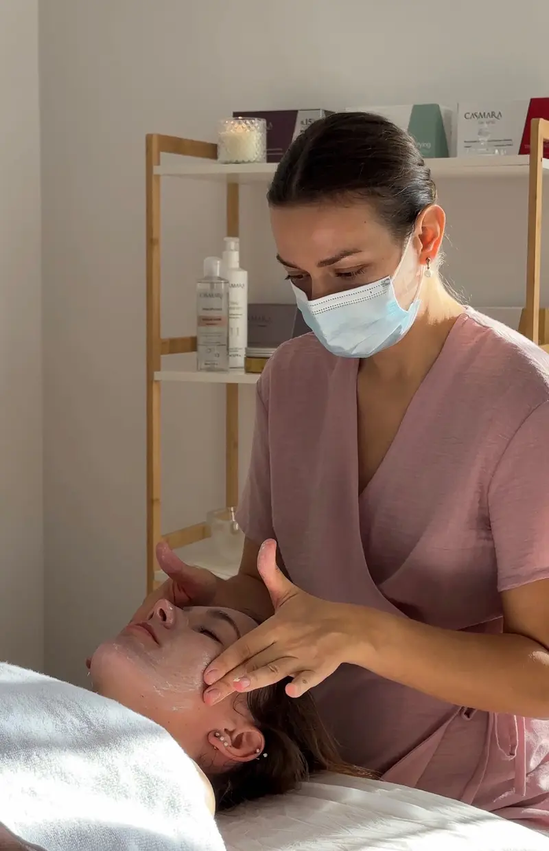 Cosmetologist performing a facial massage with Casmara skincare on the shelf behind